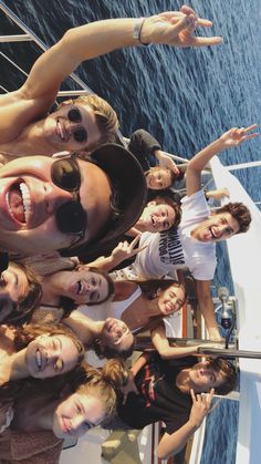 a group of people standing on top of a boat in front of the ocean with their hands up