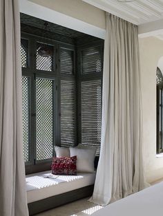 a white bed sitting next to a window covered in curtained drapes and pillows