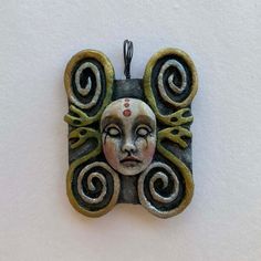 a pendant with a face on it is hanging from a cord and has swirls around the edges