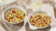 two white bowls filled with corn salad on top of a table next to a glass of water