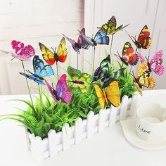 a white vase filled with lots of colorful butterflies next to a cup and saucer