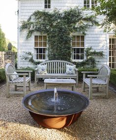 an outdoor seating area with chairs and a water fountain in front of a white house