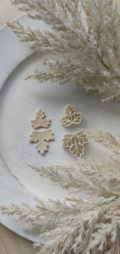 three wooden ornaments sitting on top of a white plate next to some dried plant life