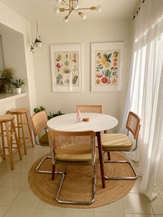 a dining room table with four chairs around it and pictures on the wall behind it