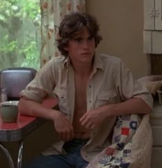 a young man sitting at a table with a cup in his hand and looking off to the side