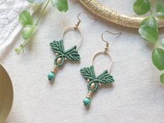 green beaded earrings sitting on top of a table next to a plate and plant