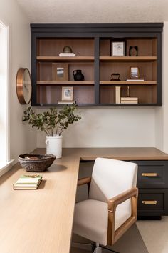 a desk with a chair, bookshelf and vase on it in front of a window