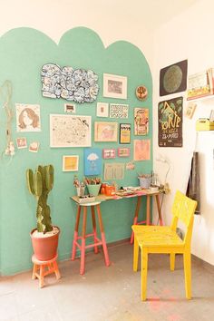 two yellow chairs are in front of a green wall with pictures on it and a cactus