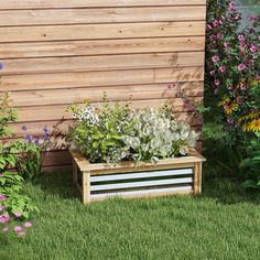 a wooden planter filled with lots of flowers next to a wall and grass field