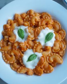 a white plate topped with macaroni and cheese covered in sour cream, garnished with green leafy leaves