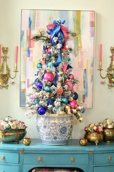 a decorated christmas tree sitting on top of a blue table in front of a painting