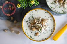 two bowls filled with food next to a yellow spoon and some flowers on the table