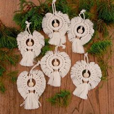 six white crocheted ornaments hanging from a pine branch on a wooden table with evergreen needles