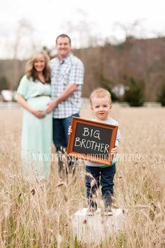 a baby holding a chalkboard with the words big brother on it in front of two adults