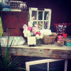 an old wooden table with flowers and other items on it, sitting in front of a window