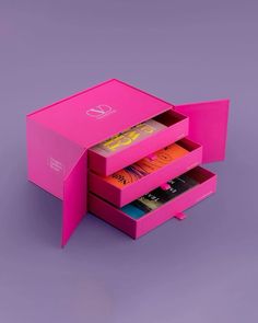 an open pink box with three different books in it on a purple surface, showing the inside compartments