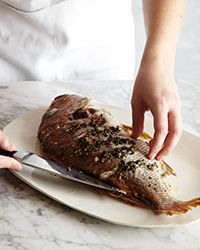 a person cutting up a fish on top of a white plate next to a knife