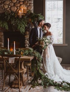 a bride and groom standing in front of a fireplace with greenery on the mantle