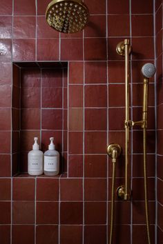 a red tiled bathroom with shower head and soap dispenser next to it