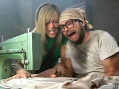 a man and woman sitting next to an old sewing machine with their mouths open while looking at the camera