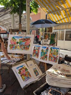 a woman looking at art on display under an umbrella in the street side market area