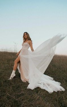 a woman sitting on top of a grass covered field wearing a white dress and boots