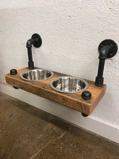 two metal bowls on wooden shelf with black faucets and pipes attached to the wall