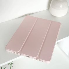 a pink ipad case sitting on top of a white table next to a vase with flowers