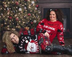 two women in matching ugly christmas sweaters pose for a photo next to a christmas tree