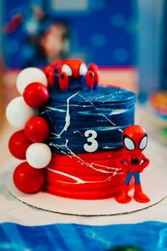 a spiderman themed birthday cake with red, white and blue decorations on it's top