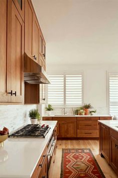 a kitchen with wooden cabinets and white counter tops, along with a red rug on the floor