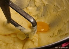 a metal bowl filled with batter and an egg being whisked by a beater