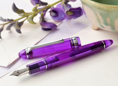 a purple fountain pen sitting on top of a table next to a vase with flowers