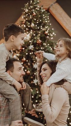 a family standing in front of a christmas tree with the child on his shoulders and an adult holding her up