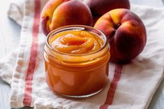 peach jam in a glass jar next to two peaches on a white and red towel