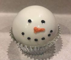 a cupcake with a frosting snowman face on it's side, sitting on a white surface