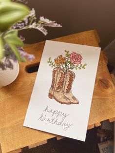 a happy birthday card with boots and flowers on it next to a potted plant