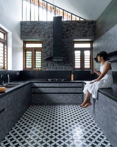 a woman sitting on the edge of a kitchen counter next to a sink and stove