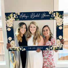 three women pose for a photo in front of a floral frame that says, ally's bridal shower