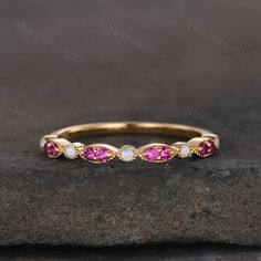 a yellow gold ring with pink and white stones on top of a stone slab in front of a rock