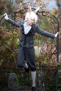 a woman with white hair and rabbit ears is posing on a fence in front of some bushes