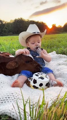 a baby sitting on a blanket with a cow and soccer ball in it's mouth