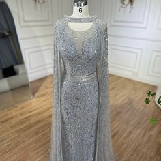 Elegant Mermaid Silhouette: Designed to beautifully enhance the feminine figure, providing a sleek and figure-hugging fit that flares out at the knees. Sophisticated Gray Hue: Crafted from high-quality fabric in a chic gray color, offering a modern and refined appearance. Intricate Beaded Detailing: Adorned with luxurious beadwork that adds a touch of opulence and sophistication. Detachable Long Cape: Features a detachable cape that provides a dramatic and versatile flair, perfect for making a g Detachable Cape, Beaded Evening Gowns, Long Cape, Bridal Elegance, Capes For Women, Stunning Gowns, Mermaid Silhouette, Ladies Party, Formal Occasion