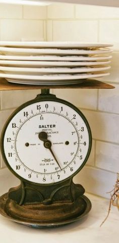 a stack of plates sitting on top of a kitchen counter next to an old scale