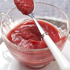 two spoons in a glass bowl filled with strawberry jam on a white saucer