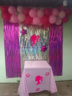 a table with pink and purple balloons on it in front of a curtained wall