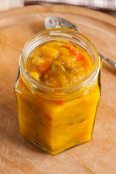 a glass jar filled with food sitting on top of a wooden cutting board next to a spoon