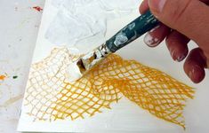 someone is using a brush to paint an orange piece of paper with white crisscrosses