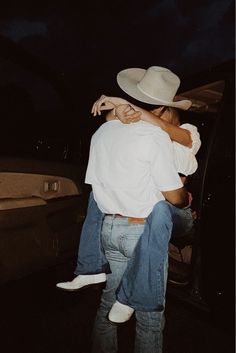 a man in a cowboy hat is being carried into a car by another man wearing jeans and a white shirt