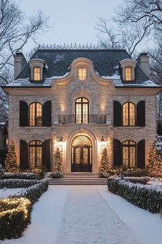 a large house with lots of windows and lights on it's front door in the snow